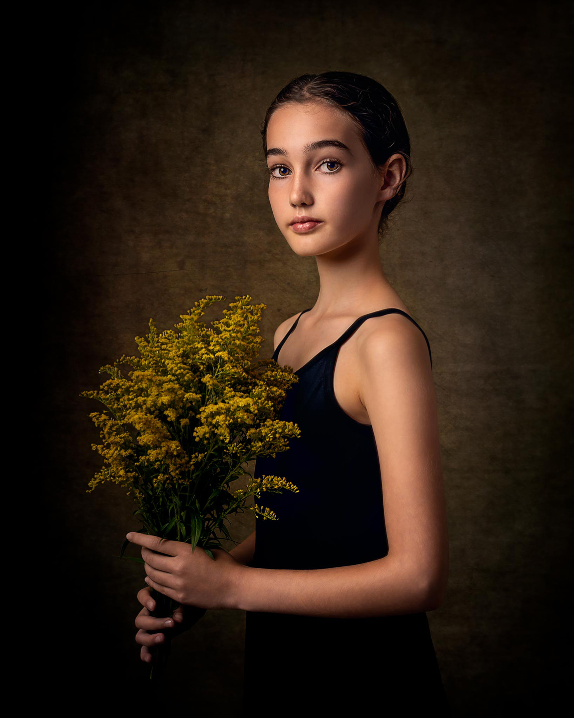 niña sosteniendo flores cafés con fondo café oscuro viendo a cámara